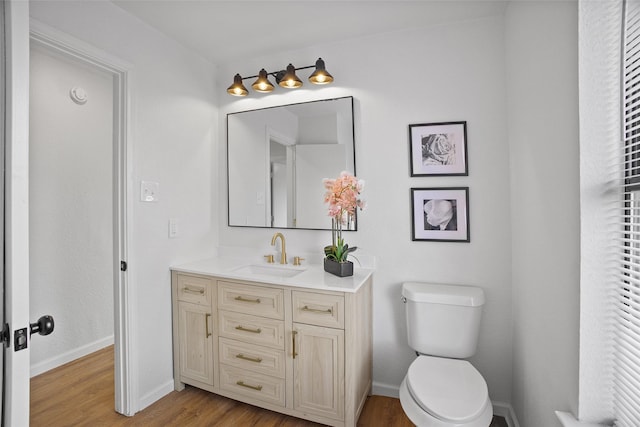 bathroom with toilet, vanity, baseboards, and wood finished floors