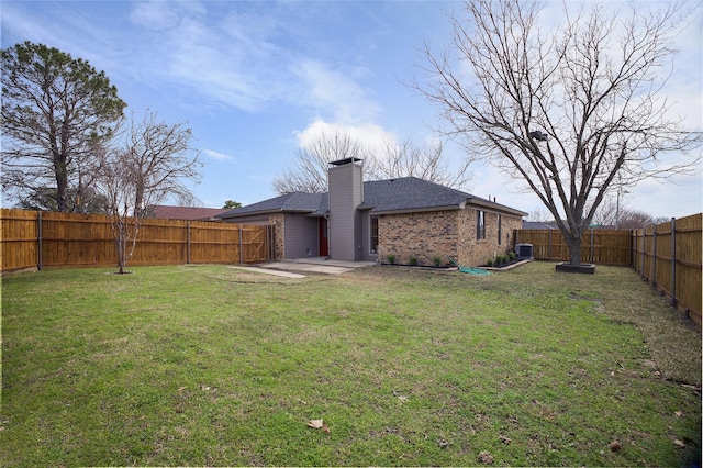 back of house featuring central AC unit, a fenced backyard, a chimney, a yard, and brick siding