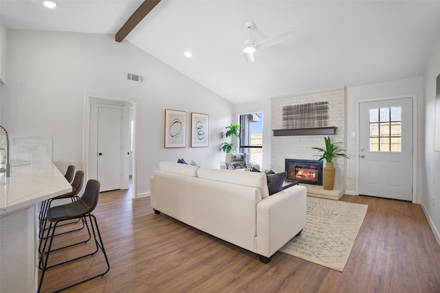 living room featuring visible vents, beam ceiling, a brick fireplace, and a wealth of natural light