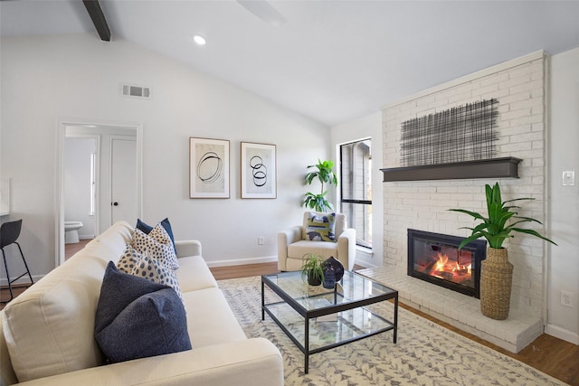 living area with a fireplace, vaulted ceiling with beams, and wood finished floors