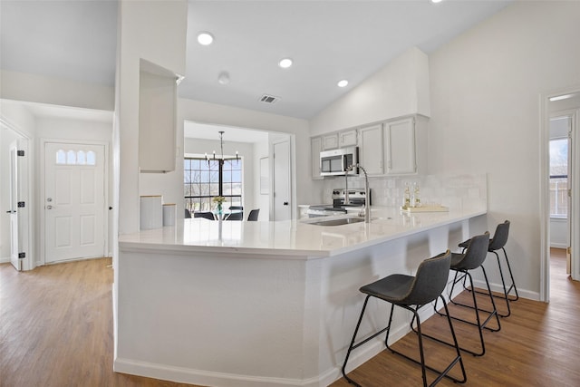 kitchen with vaulted ceiling, stainless steel appliances, a peninsula, and visible vents