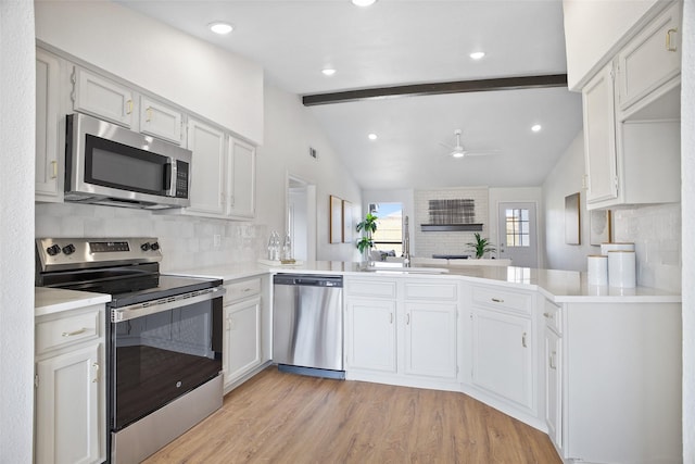 kitchen featuring lofted ceiling with beams, a ceiling fan, light wood-style floors, appliances with stainless steel finishes, and tasteful backsplash