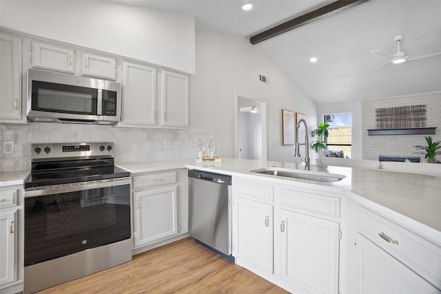 kitchen featuring stainless steel appliances, lofted ceiling with beams, decorative backsplash, light wood-style floors, and a sink