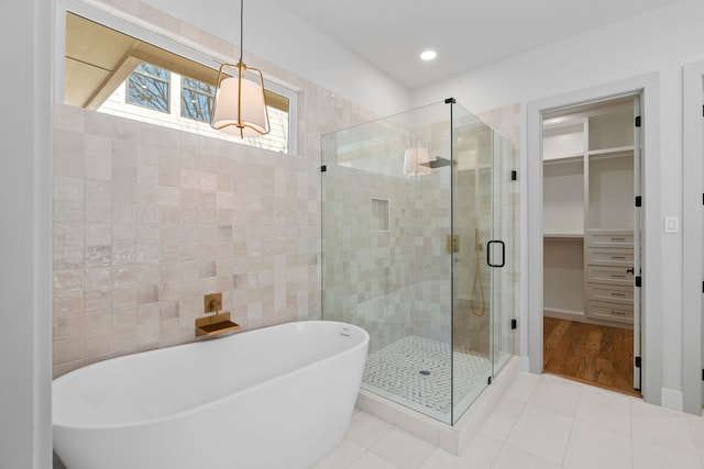 bathroom featuring a walk in closet, tile walls, a soaking tub, a shower stall, and tile patterned flooring