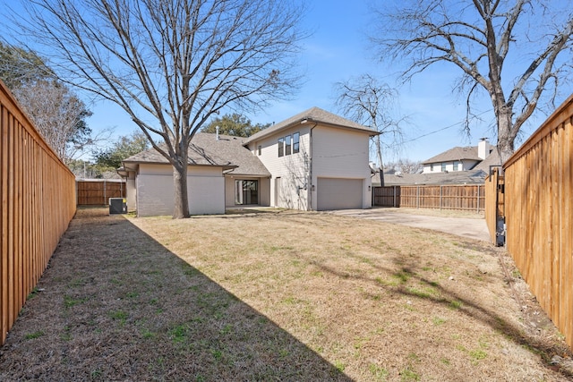 back of property with driveway, central air condition unit, a fenced backyard, and a yard