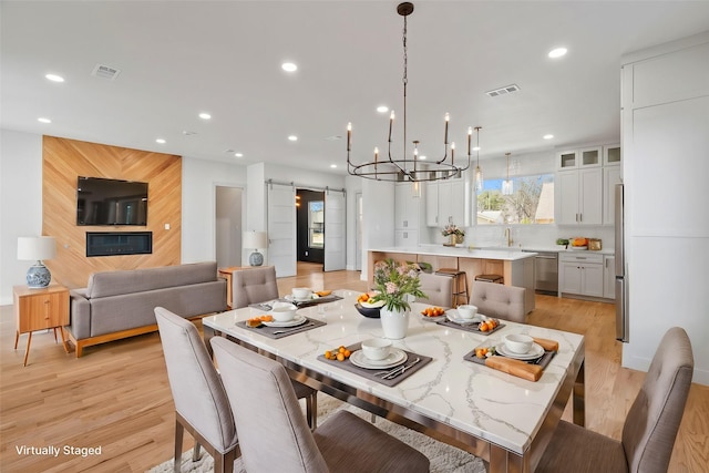 dining area with a barn door, light wood-style flooring, visible vents, and recessed lighting