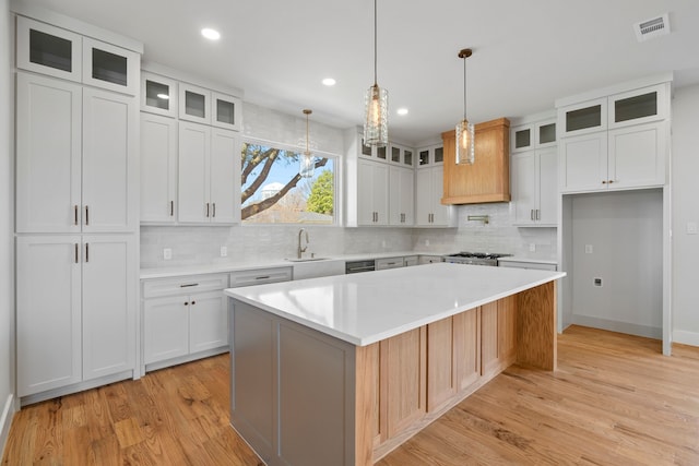 kitchen with light wood finished floors, visible vents, white cabinets, a kitchen island, and light countertops