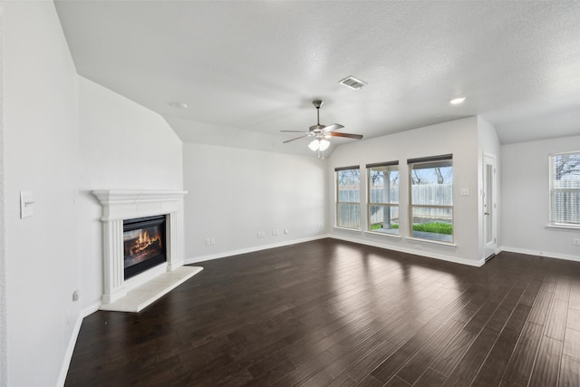 unfurnished living room featuring baseboards, visible vents, dark wood finished floors, a glass covered fireplace, and ceiling fan