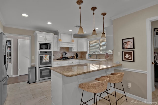 kitchen with a breakfast bar area, backsplash, appliances with stainless steel finishes, a sink, and a peninsula