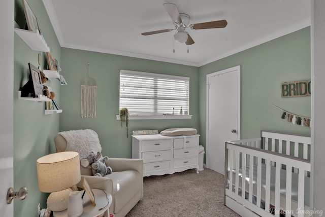 carpeted bedroom featuring a crib, ceiling fan, and crown molding