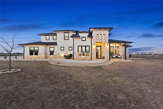 rear view of property featuring stone siding, fence, and stucco siding