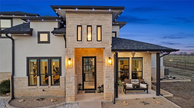 rear view of property featuring stone siding, roof with shingles, cooling unit, and stucco siding