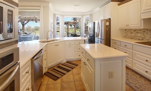 kitchen with stainless steel appliances, tasteful backsplash, an inviting chandelier, a sink, and a kitchen island