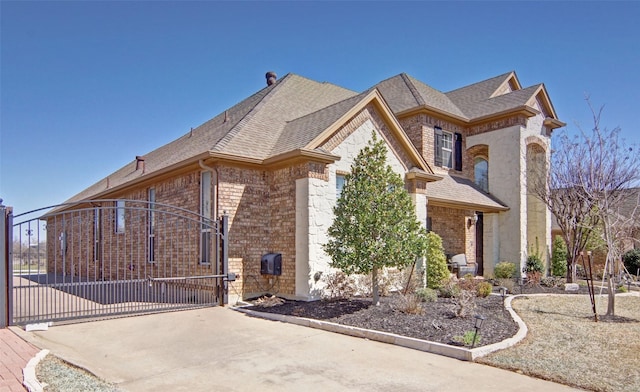 view of property exterior featuring roof with shingles, a gate, concrete driveway, and brick siding