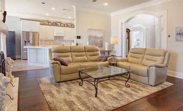 living area with a ceiling fan, arched walkways, dark wood finished floors, and crown molding