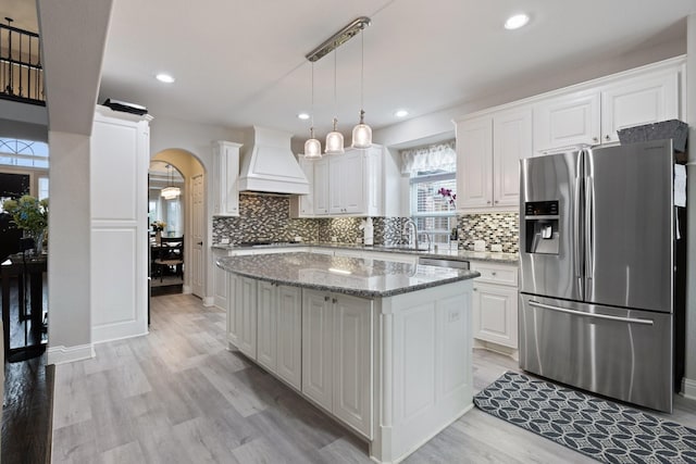 kitchen with arched walkways, custom range hood, appliances with stainless steel finishes, white cabinetry, and a sink