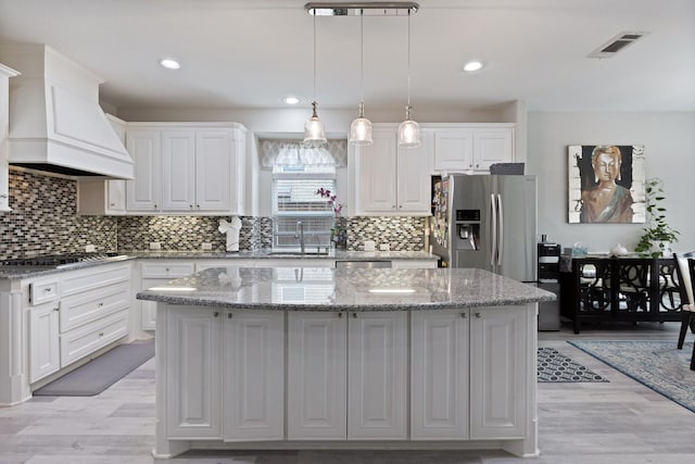 kitchen featuring visible vents, a kitchen island, custom range hood, appliances with stainless steel finishes, and a sink