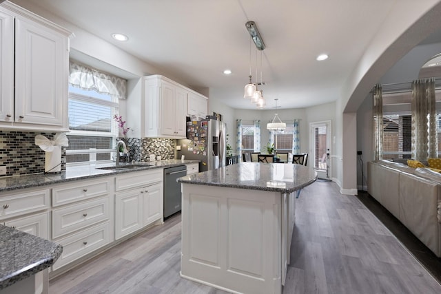 kitchen featuring appliances with stainless steel finishes, arched walkways, white cabinetry, and a sink