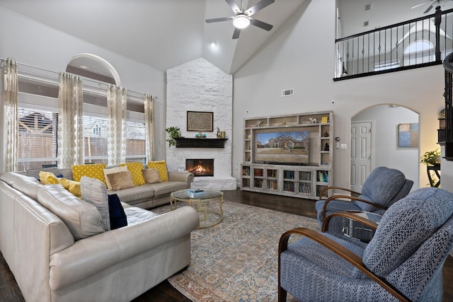 living area featuring arched walkways, ceiling fan, a stone fireplace, wood finished floors, and visible vents