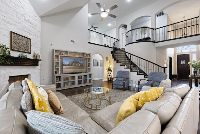 living room with arched walkways, a stone fireplace, wood finished floors, visible vents, and stairs