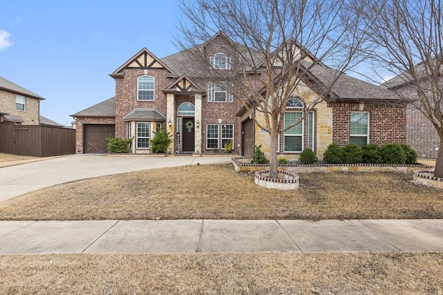 view of front facade with brick siding, roof with shingles, an attached garage, fence, and driveway