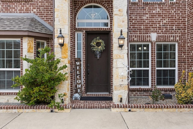 property entrance featuring a shingled roof and brick siding