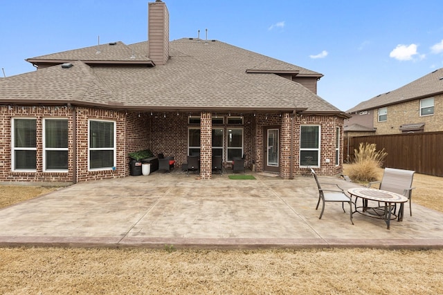 rear view of property featuring a shingled roof, brick siding, a patio, and fence