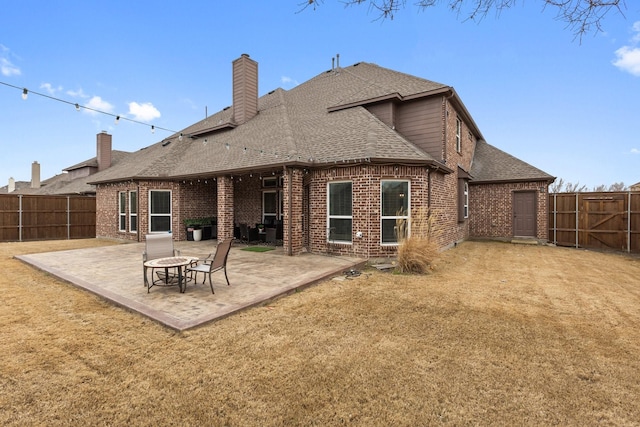 back of property with brick siding, roof with shingles, a fenced backyard, and a patio