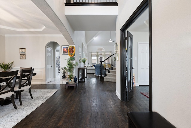 entryway with arched walkways, wood finished floors, stairs, and ornamental molding