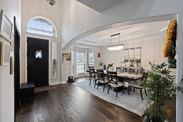 foyer featuring dark wood-style floors, arched walkways, a chandelier, and a tray ceiling