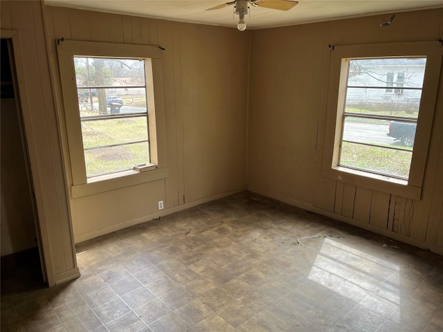 unfurnished room featuring light floors, ceiling fan, and wooden walls