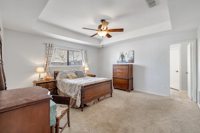 bedroom with a tray ceiling, light carpet, visible vents, and baseboards