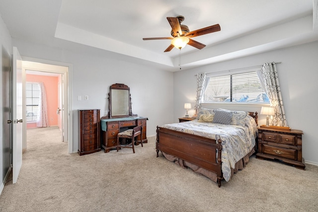 carpeted bedroom featuring ceiling fan, a tray ceiling, and baseboards