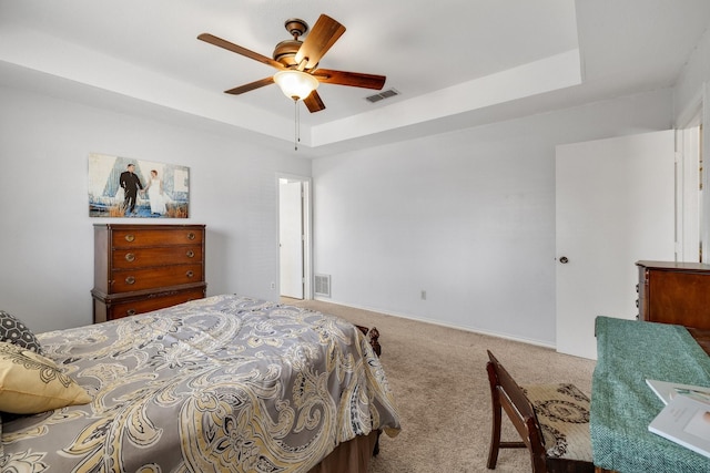 bedroom featuring carpet floors, a tray ceiling, visible vents, and a ceiling fan