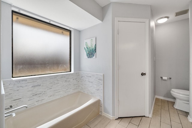 bathroom featuring toilet, a garden tub, baseboards, and visible vents