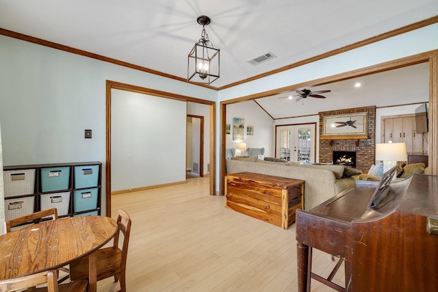 living area with light wood-style flooring, ceiling fan with notable chandelier, a fireplace, visible vents, and ornamental molding