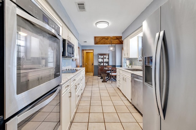 kitchen featuring light tile patterned floors, stainless steel appliances, a sink, visible vents, and white cabinets