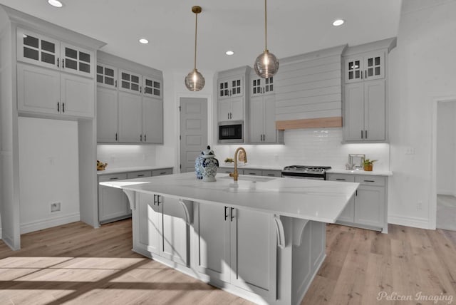 kitchen with stainless steel appliances, a sink, light countertops, light wood-type flooring, and a center island with sink