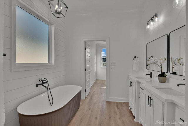 bathroom with double vanity, a freestanding bath, a sink, and wood finished floors