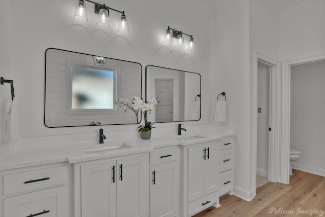 full bath with double vanity, toilet, a sink, and wood finished floors