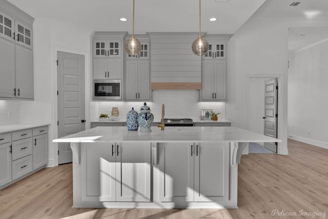 kitchen featuring a breakfast bar area, light wood-style flooring, ornamental molding, light stone countertops, and built in microwave