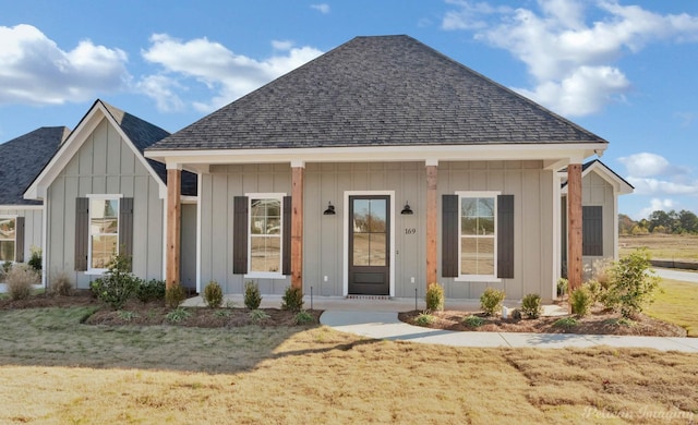 view of front facade with covered porch, roof with shingles, a front lawn, and board and batten siding