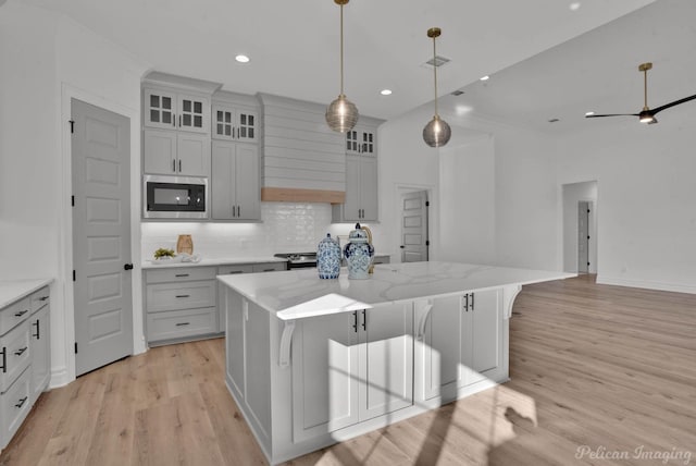 kitchen featuring pendant lighting, stainless steel appliances, backsplash, a kitchen island, and light wood-type flooring