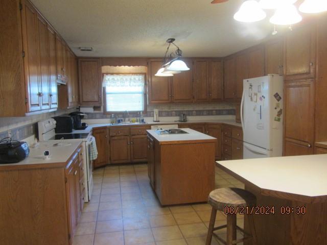 kitchen with light countertops, brown cabinetry, a kitchen island, white appliances, and a kitchen breakfast bar