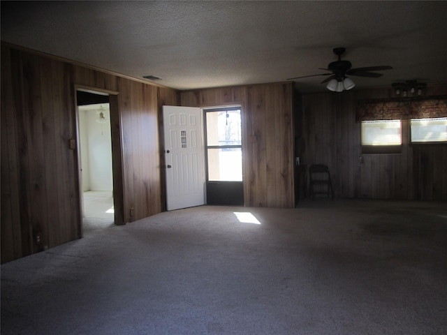 unfurnished living room featuring a textured ceiling, wood walls, carpet, and visible vents