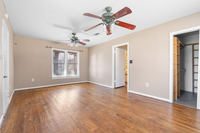 unfurnished bedroom with a walk in closet, wood finished floors, visible vents, and baseboards