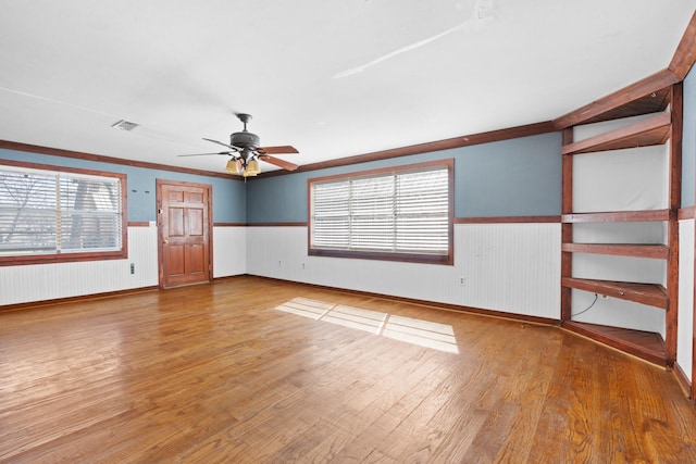 unfurnished room featuring visible vents, a ceiling fan, wainscoting, ornamental molding, and wood finished floors