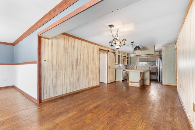 unfurnished living room featuring baseboards, a barn door, ornamental molding, and dark wood-type flooring