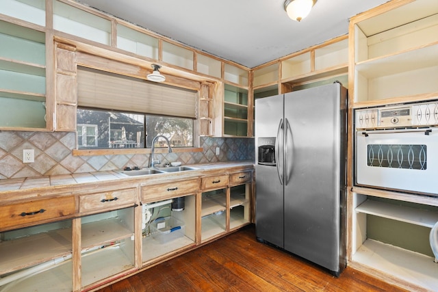 kitchen with stainless steel fridge, dark wood-style flooring, oven, a sink, and backsplash