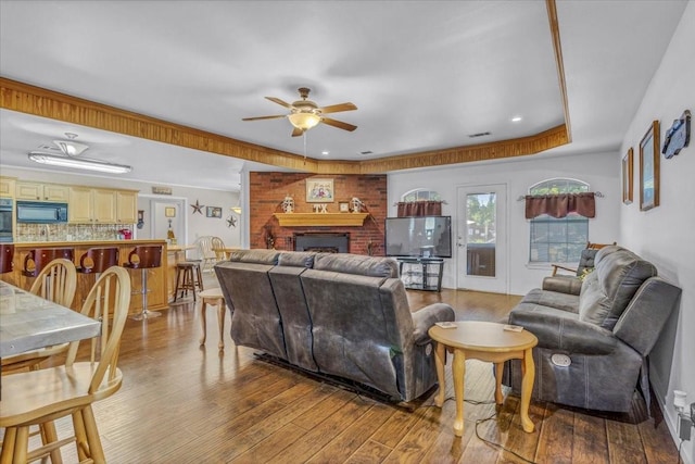 living room featuring a brick fireplace, ceiling fan, and wood finished floors